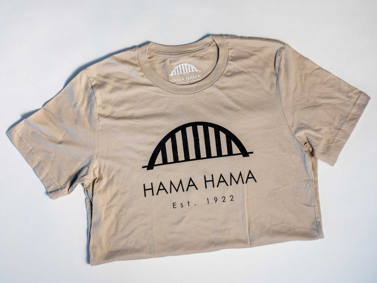 a silhouette of the tan Hama Hama Oyster Company bridge logo tee shirt in a folded position