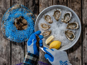 action photo of a person shucking blue pool oysters and placing them on the half shell on a serving tray filled with ice and a lemon